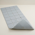A light gray rectangular mat with a grid of raised square sections and a folded corner revealing a textured underside, photographed on a plain light background.