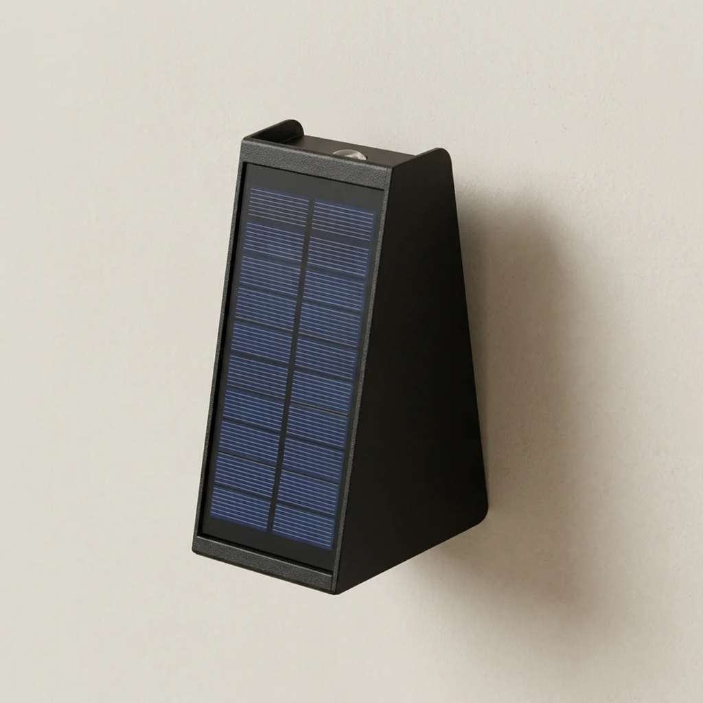 A wall-mounted triangular solar lantern with a blue solar panel on a black housing, shown against a plain beige wall.