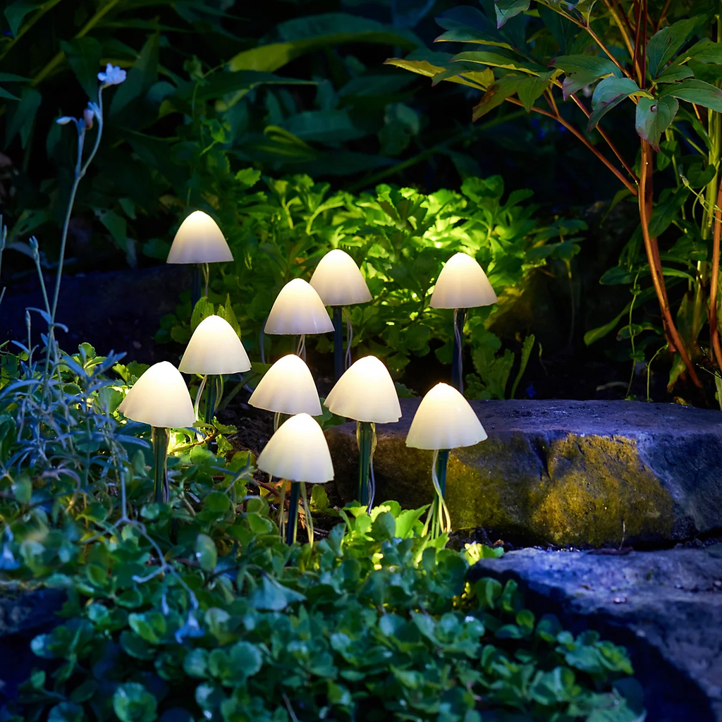 A group of small mushroom-shaped outdoor lights glowing in a garden setting among green plants and a stone path.