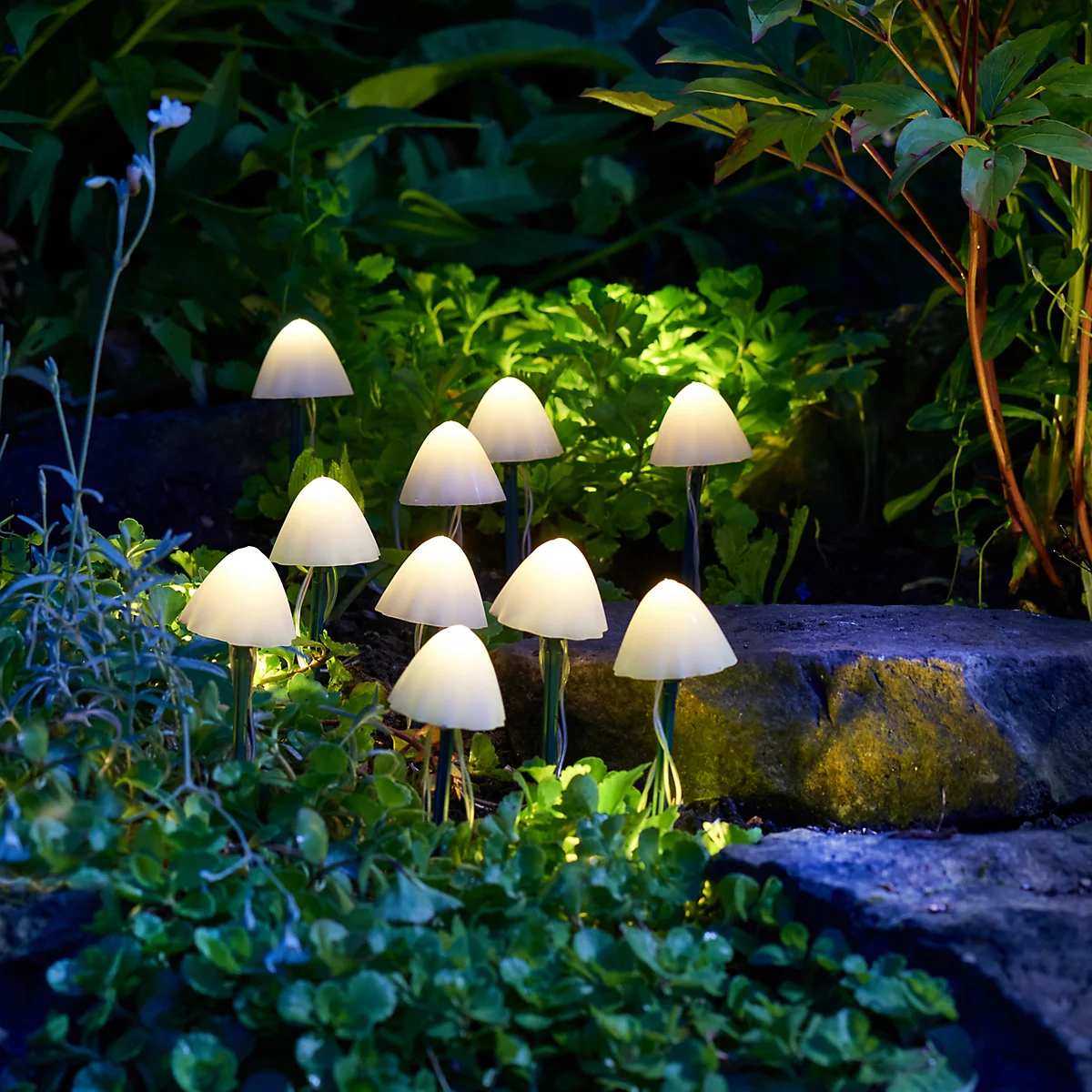 A group of small mushroom-shaped outdoor lights glowing in a garden setting among green plants and a stone path.