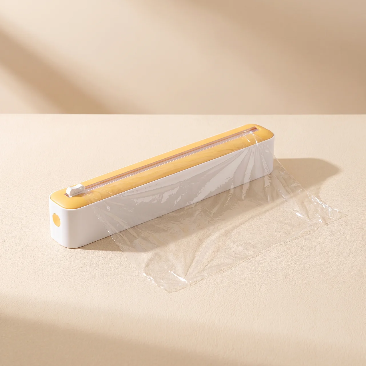 A clear plastic wrap sealer tool with a white body and yellow top, shown sealing clear plastic wrap on a beige surface with soft shadows.