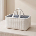 A white corduroy storage basket with fabric handles and a navy blue striped interior, sitting on a beige fabric-covered surface.