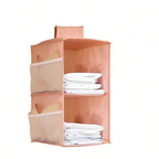 A peach-colored fabric hanging organizer with mesh side pockets and two open shelves, shown holding folded white towels or sheets against a plain white background.