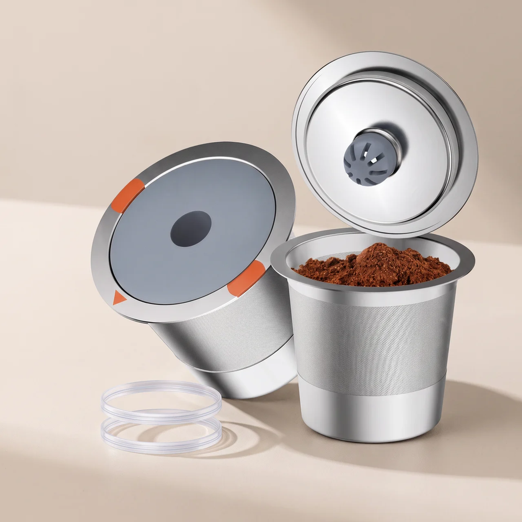 A stainless steel coffee capsule filling machine shown disassembled with its lid, inner capsule, and clear plastic seal on a warm beige background.