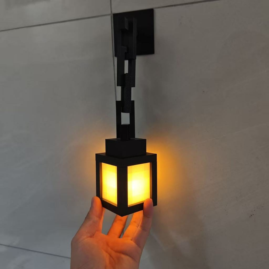 A black modern wall sconce with a glowing warm yellow light, held by a hand against a light gray tiled wall.