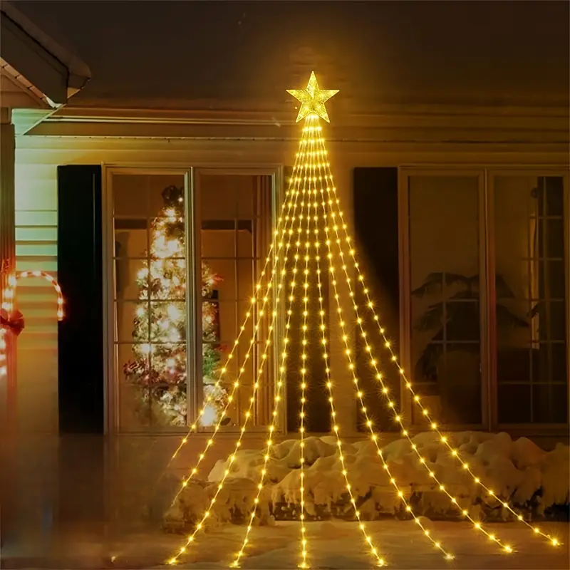 A glowing Christmas tree light display with a star topper, strung vertically and fanned out across a snowy ground in front of a house at night.