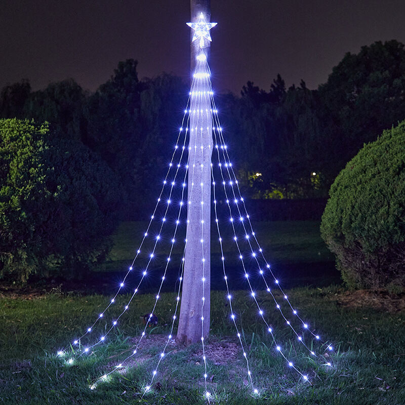 A string light Christmas tree decoration with a star topper, draped over a wooden pole outdoors at night, casting a bright blue-white glow on the grass and shrubs.