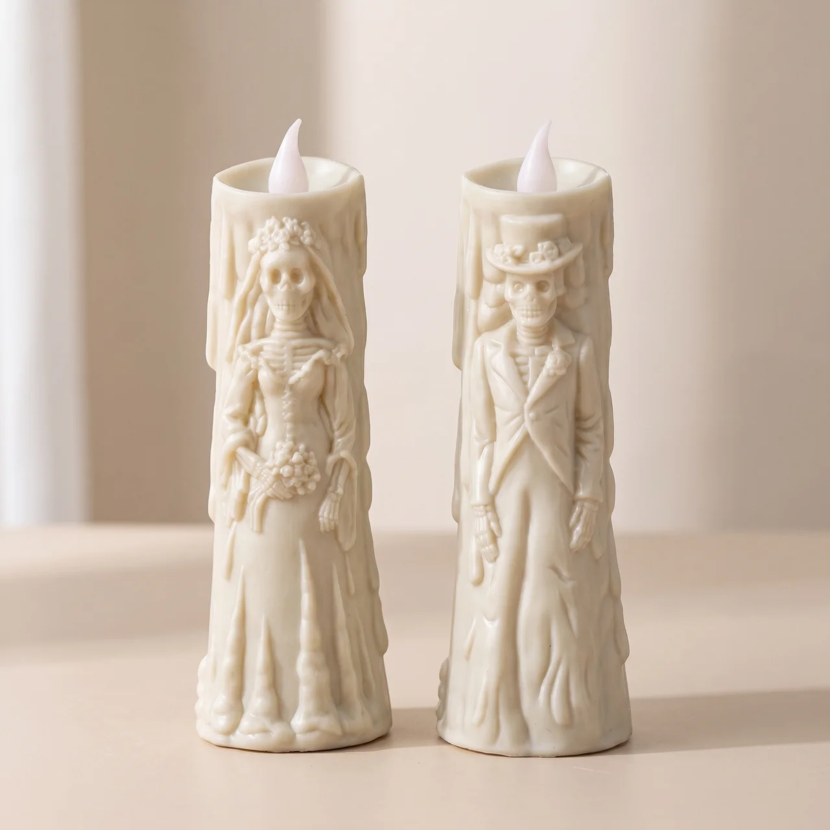 Two cream-colored LED taper candles shaped like skeleton bride and groom figures, standing side by side on a light beige surface against a soft neutral background.