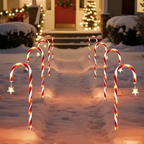 Outdoor holiday yard decorations featuring multiple red and white striped candy cane lights with glowing warm white star accents, arranged in rows on a snowy path leading to a decorated house at night.