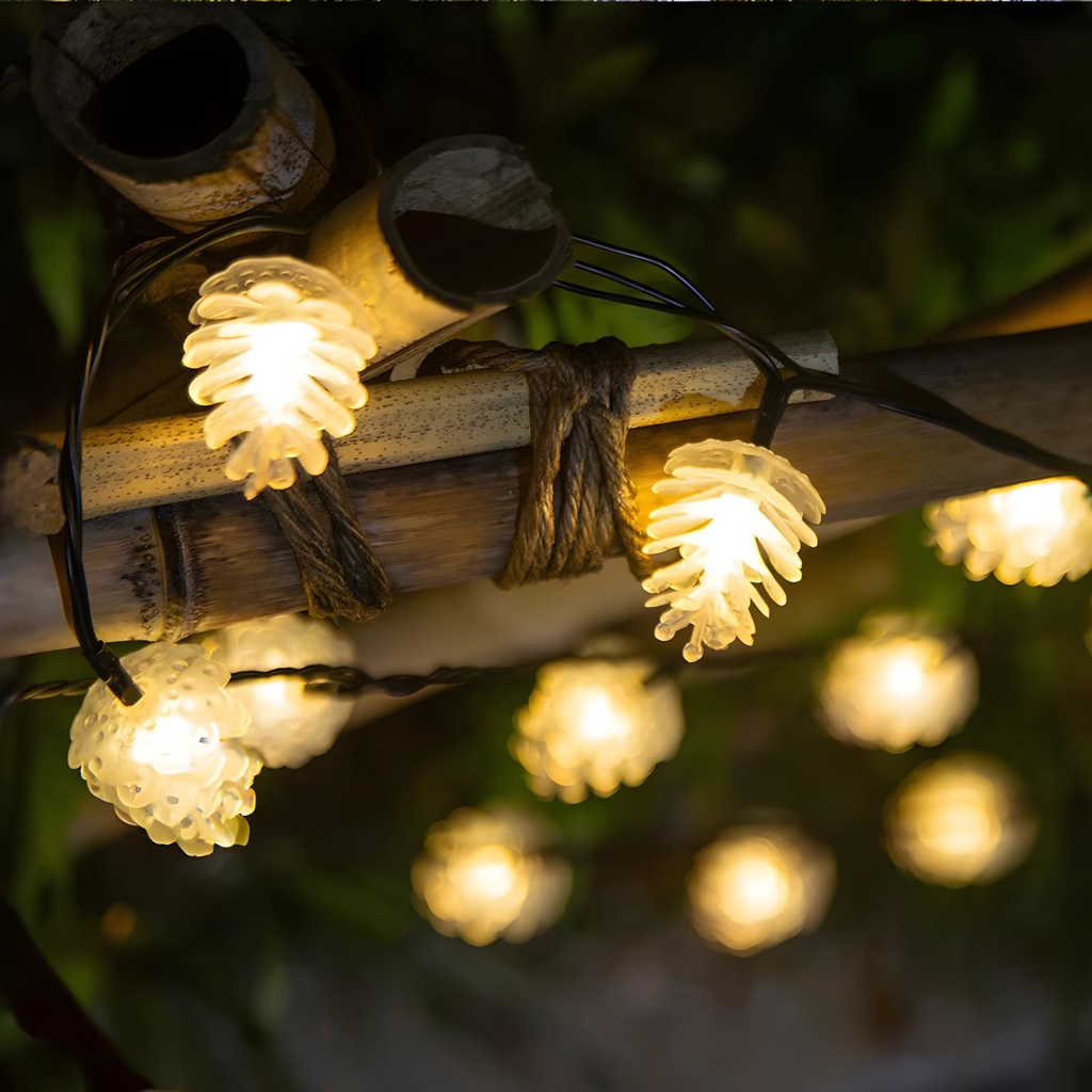 Warm white pinecone-shaped string lights wrapped around a bamboo pole outdoors, with more lights blurred in the background against dark foliage.