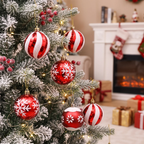 Red and white striped and snowflake Christmas tree ornaments hanging on a flocked Christmas tree in a cozy living room setting with a fireplace and stockings in the background.