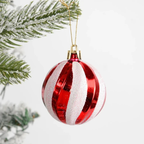 A red and white striped Christmas ornament with glittery white stripes, hanging from a gold string near a frosted green pine branch against a white background.