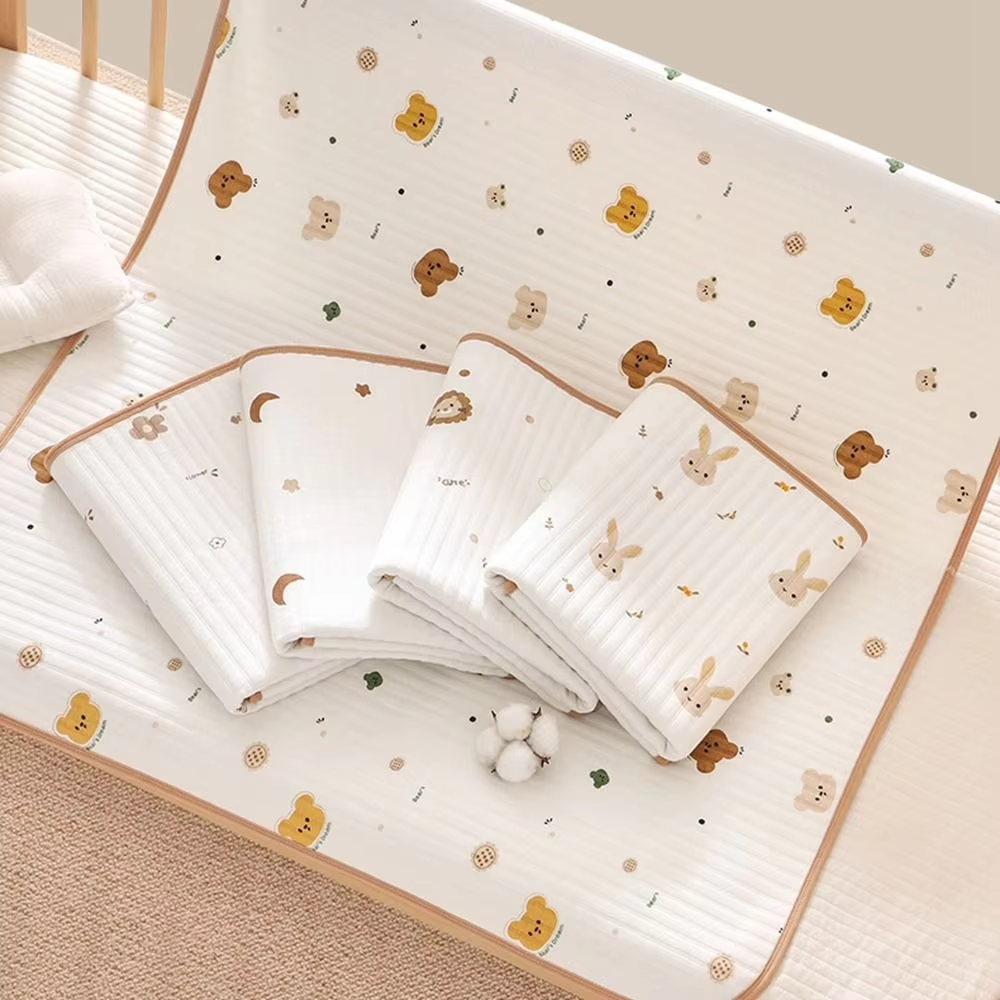 A set of baby bedding items including a large quilted mattress protector and three folded blankets, all featuring a cute cartoon animal print with bears, rabbits, and moons on a white background with a beige border.