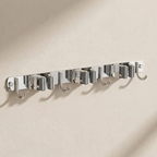 A wall-mounted silver metal hook rack with six hooks, shown mounted on a textured beige wall with soft shadows.
