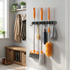 A wall-mounted multi-hook cleaning tool organizer holding several household cleaning supplies, including a broom, mop, duster, brush, and cloth, in a bright room with a bench, window, and hanging coats.