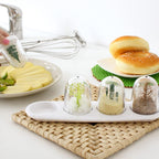 Three glass dome terrariums on a white tray, with sliced cheese, sandwiches, whisk, faucet, and woven placemat
