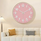 A round pink wall clock with white numerals and hands, mounted on a beige wall above a white sofa with decorative pillows.