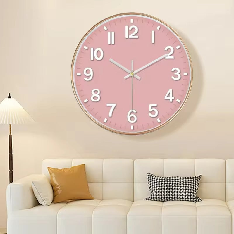 A round pink wall clock with white numerals and hands, mounted on a beige wall above a white sofa with decorative pillows.