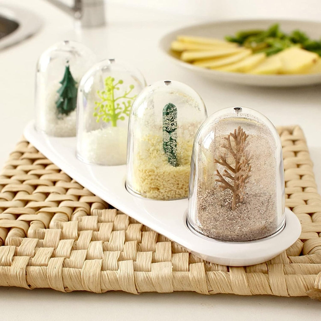 Four glass dome terrariums with miniature plants on a white tray, woven placemat, and plate of food