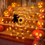A large black spiderweb decoration with warm white LED string lights draped across wooden steps, surrounded by carved jack-o'-lantern pumpkins.