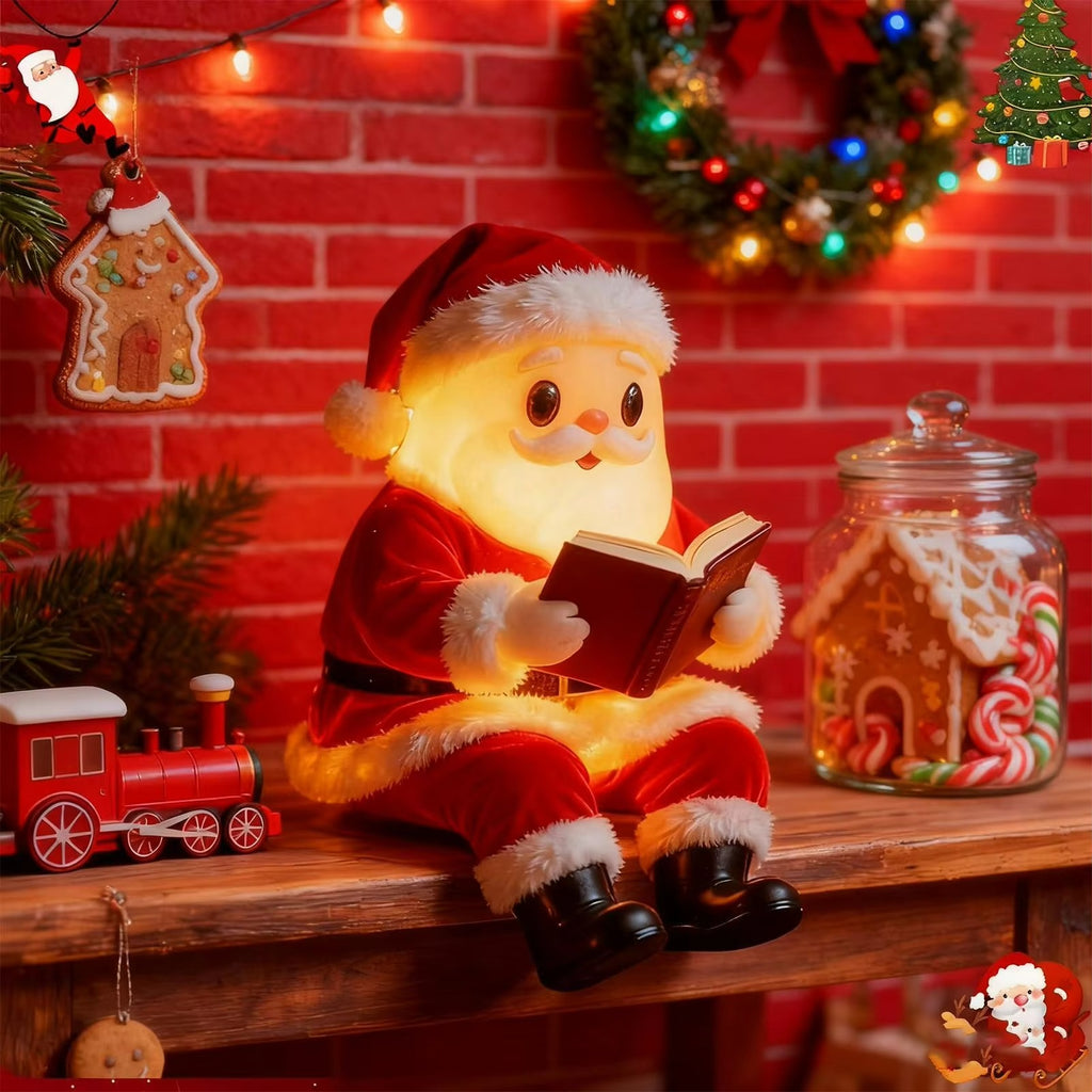 A Santa Claus plush doll wearing a red suit and hat, sitting on a wooden shelf and reading a glowing book. The scene is decorated for Christmas with a red brick wall background, warm string lights, a gingerbread house ornament, a small red toy train, and a glass jar filled with candy canes and gingerbread cookies.