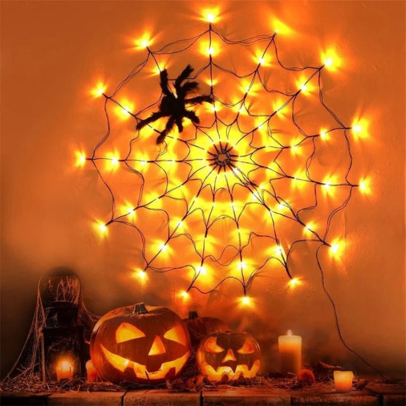 A large Halloween spiderweb decoration made of black string with many warm yellow string lights, shown hanging on a wall above carved pumpkins and candles.