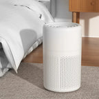 White cylindrical air purifier on a carpeted floor next to a bed in a bedroom.
