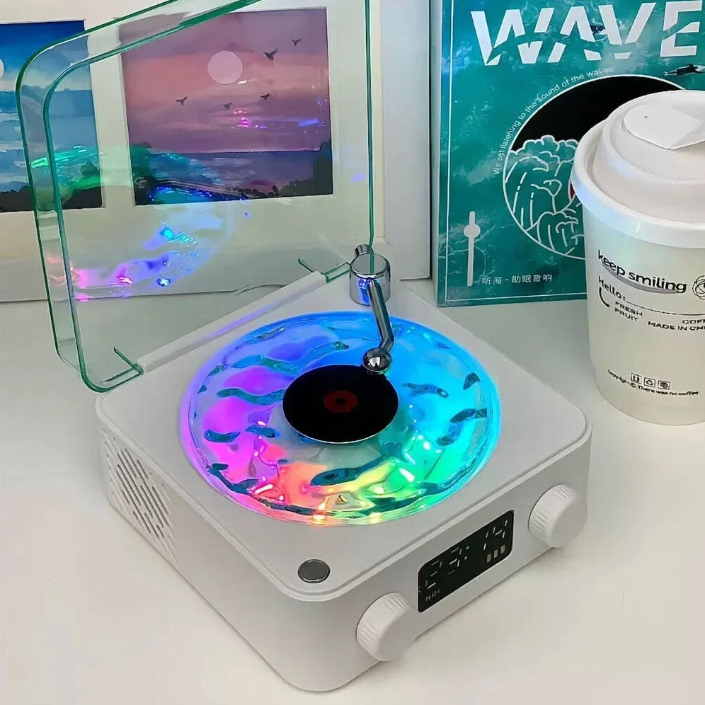 Small turntable with colorful LED lights on a white surface, surrounded by framed pictures and a container.