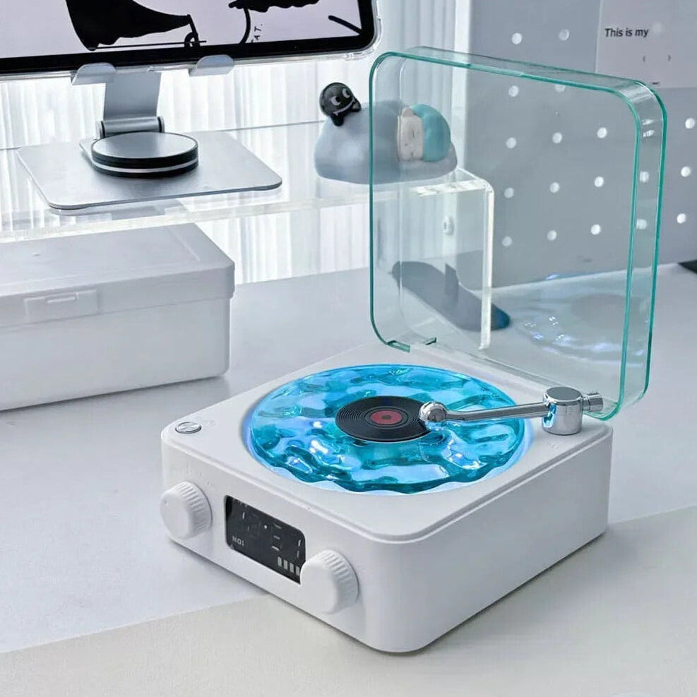 Modern record player with a transparent turntable on a white surface, with a computer monitor in the background.