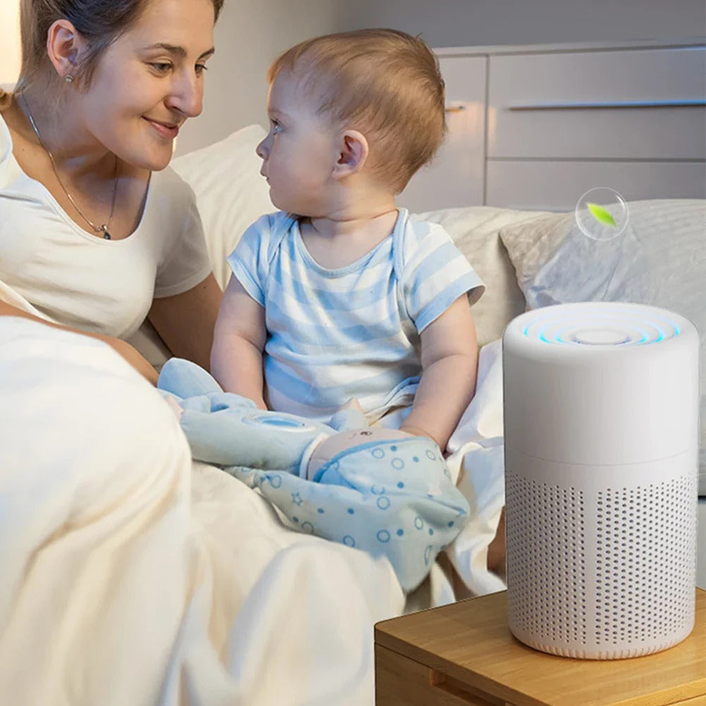 Woman and baby sitting on a couch with an air purifier on a table next to them.