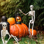 Three white plastic skeleton Halloween decorations posed around orange pumpkins and black lanterns outdoors on grass in front of green foliage.