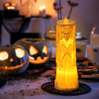 Decorative candle with skeleton design on a Halloween-themed table with pumpkins and cookies.