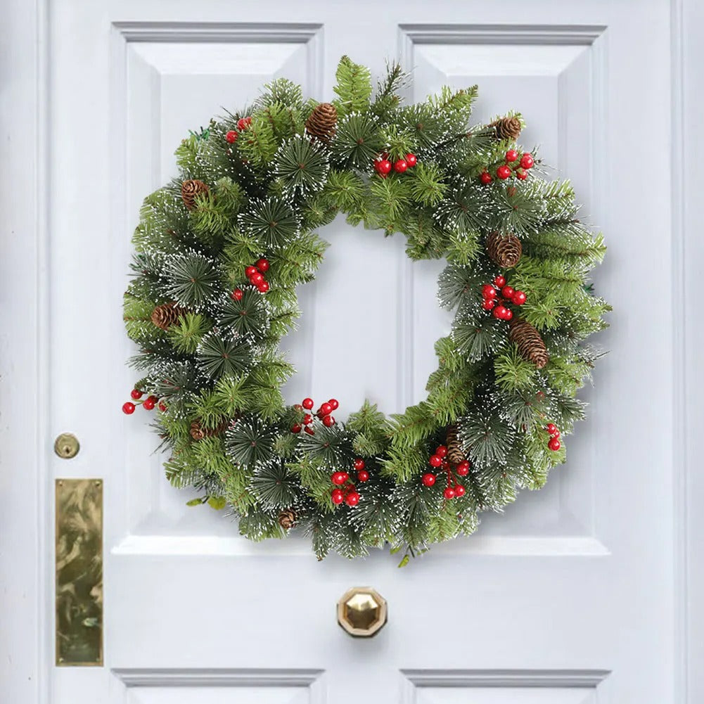 Christmas wreath with greenery, red berries, and pinecones on a white door.