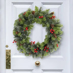 Christmas wreath with greenery, red berries, and pinecones on a white door.