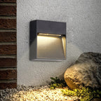 Outdoor wall light fixture on a textured wall with a rock and gravel in the foreground