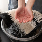 Person holding water over a pot with a towel on a stove