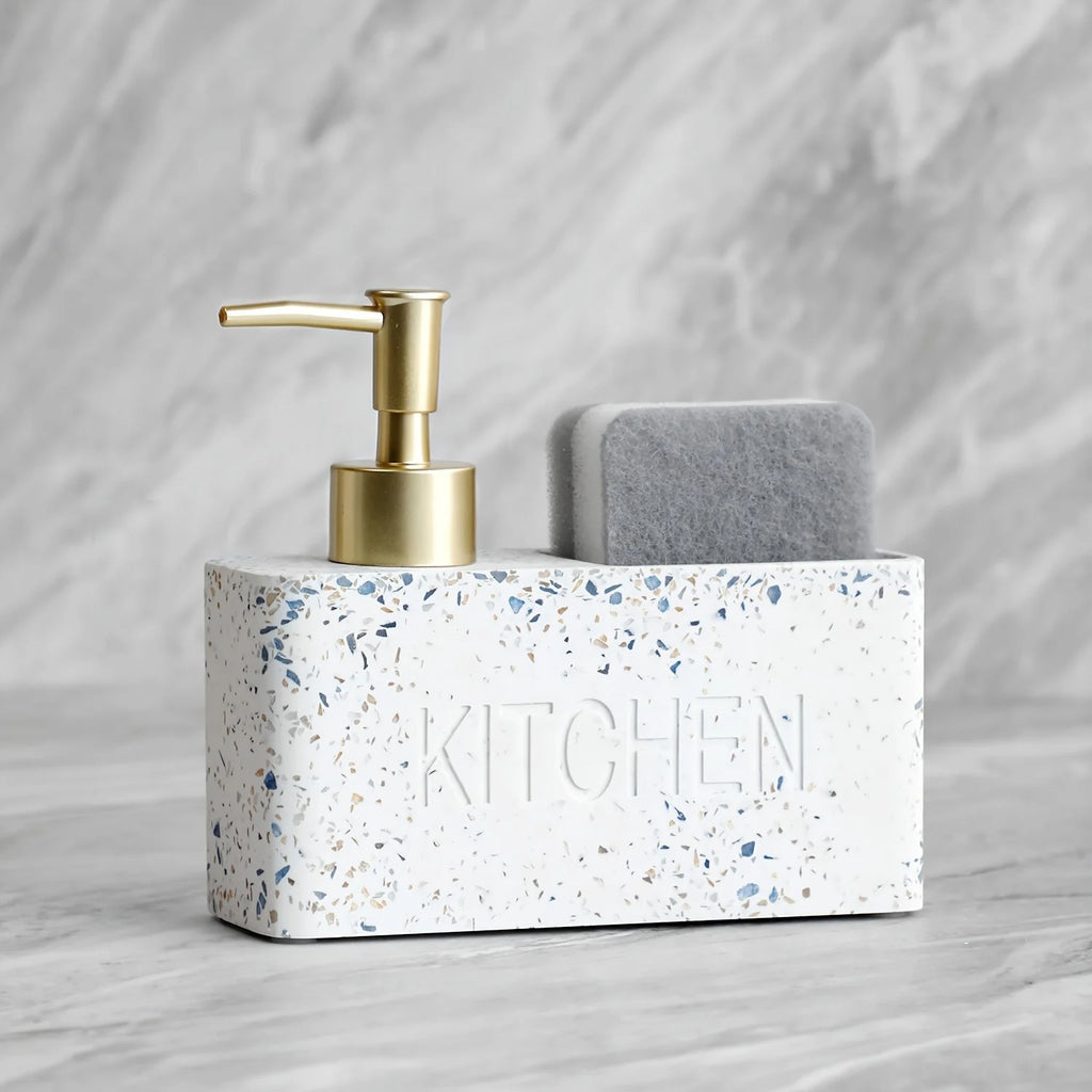White terrazzo kitchen sink caddy with gold pump and gray sponge on a marble background
