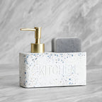 White terrazzo kitchen sink caddy with gold pump and gray sponge on a marble background