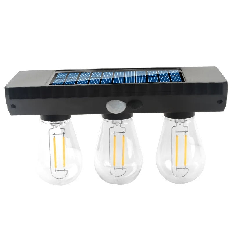 A three-light solar-powered outdoor wall sconce with a rectangular black housing, a blue solar panel on top, and three clear glass light bulbs with visible yellow filaments, shown on a white background.