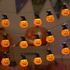 Halloween string lights featuring glowing orange jack-o'-lantern pumpkins wearing black witch hats, shown hanging against a softly blurred indoor background with more pumpkins visible.