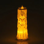 A glowing LED battery-operated pillar candle shaped like a bride with a skull face, emitting a warm yellow light against a dark background.