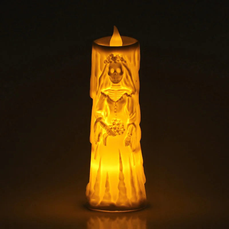 A glowing LED battery-operated pillar candle shaped like a bride with a skull face, emitting a warm yellow light against a dark background.