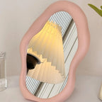 Pink mirror reflecting a lamp on a white surface with a neutral background