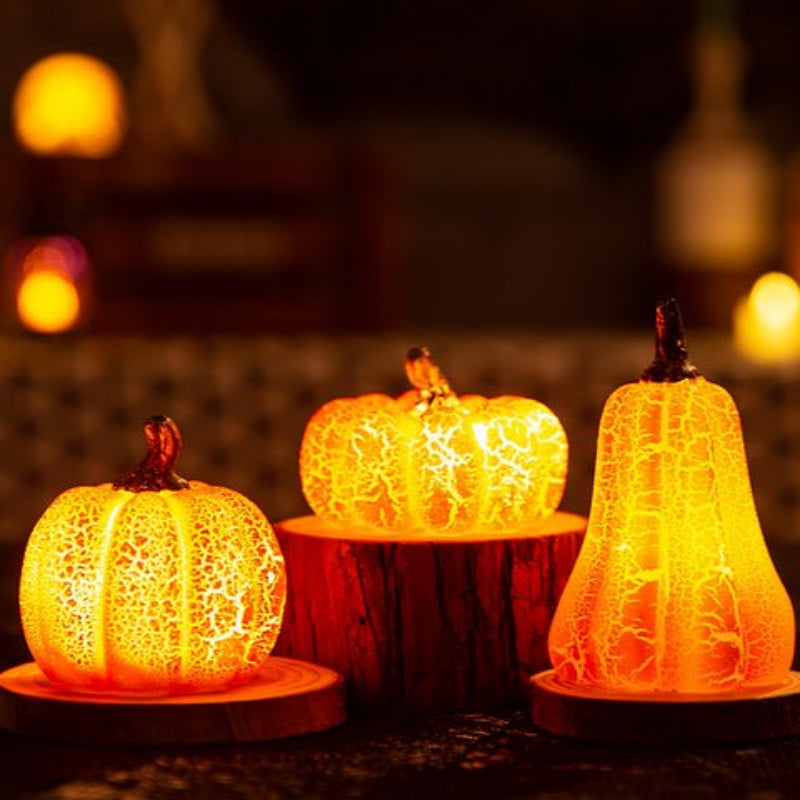 Three illuminated pumpkin-shaped lights on a dark background with blurred lights in the background
