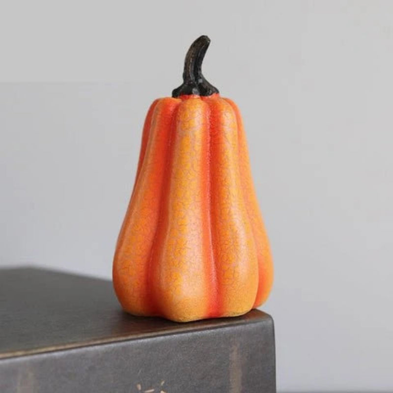 An orange and yellow striped faux pumpkin figurine with a dark stem, displayed on a dark gray block against a light gray background.