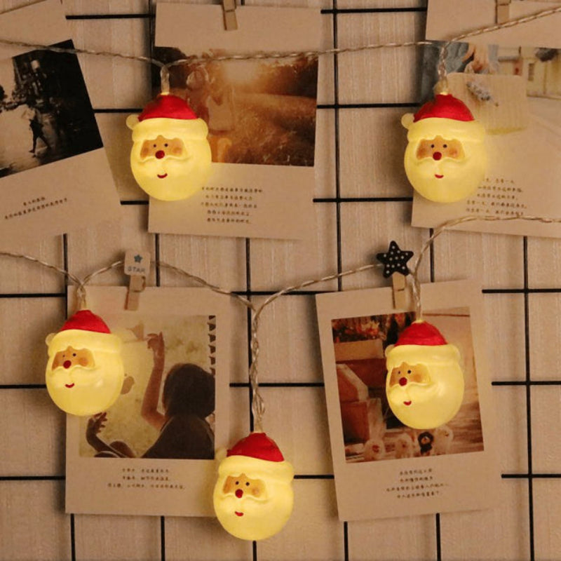 String lights with Santa Claus design hanging on a wall with photos and notes.
