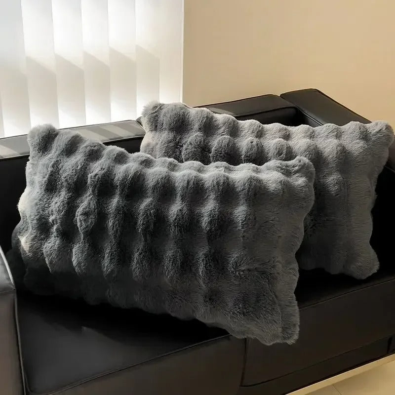 Two textured gray pillows on a dark surface with a blurred background