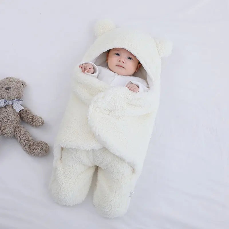 Baby wrapped in a white fluffy blanket with a teddy bear on a light gray background