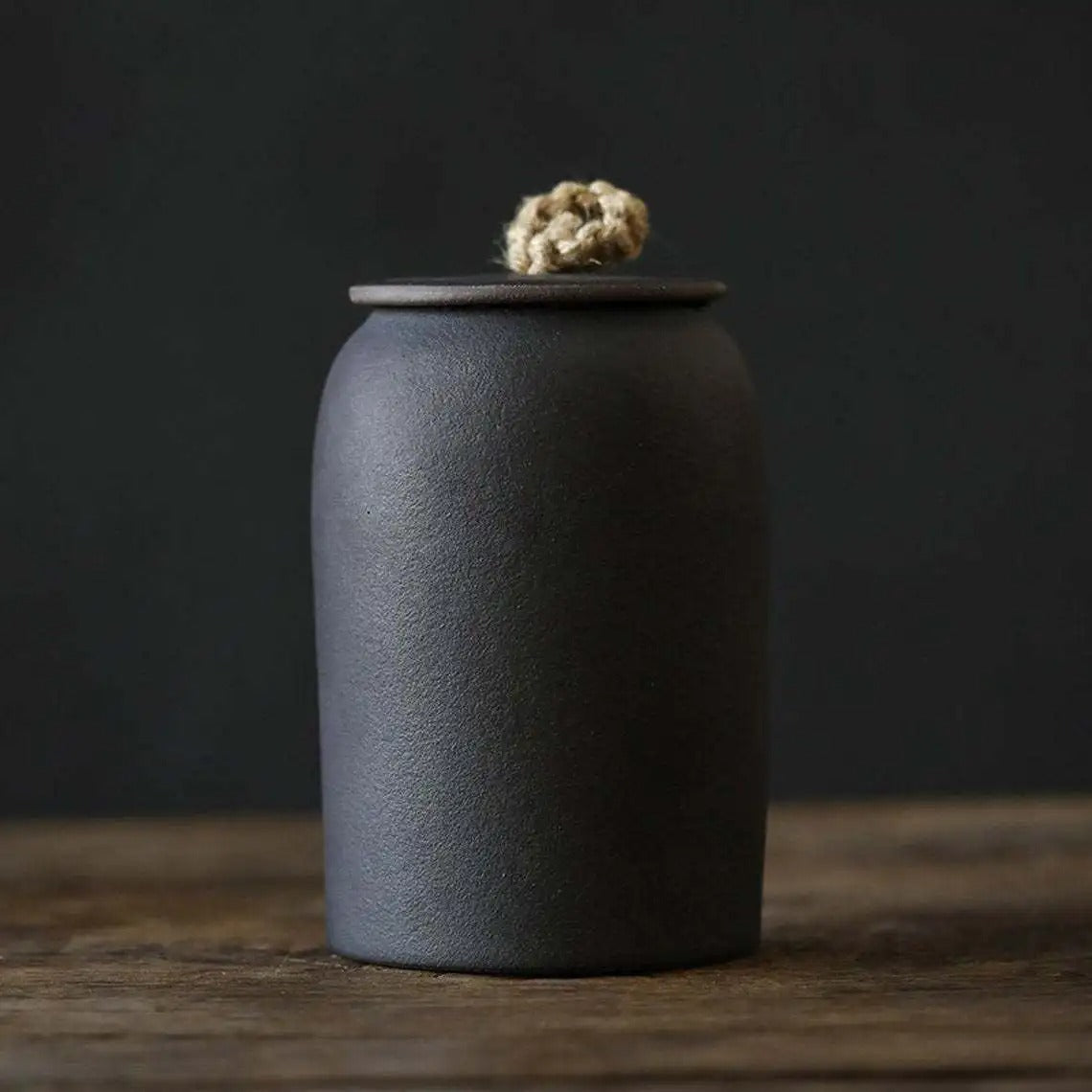 Dark gray ceramic jar with a textured lid on a wooden surface and dark background