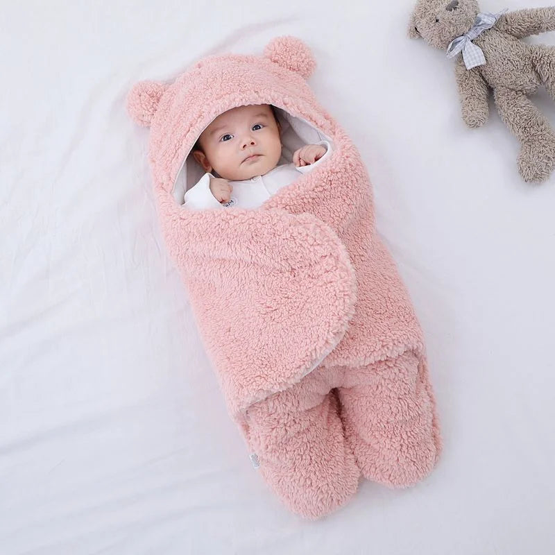 Baby wrapped in a pink fluffy blanket with bear ears on a white background